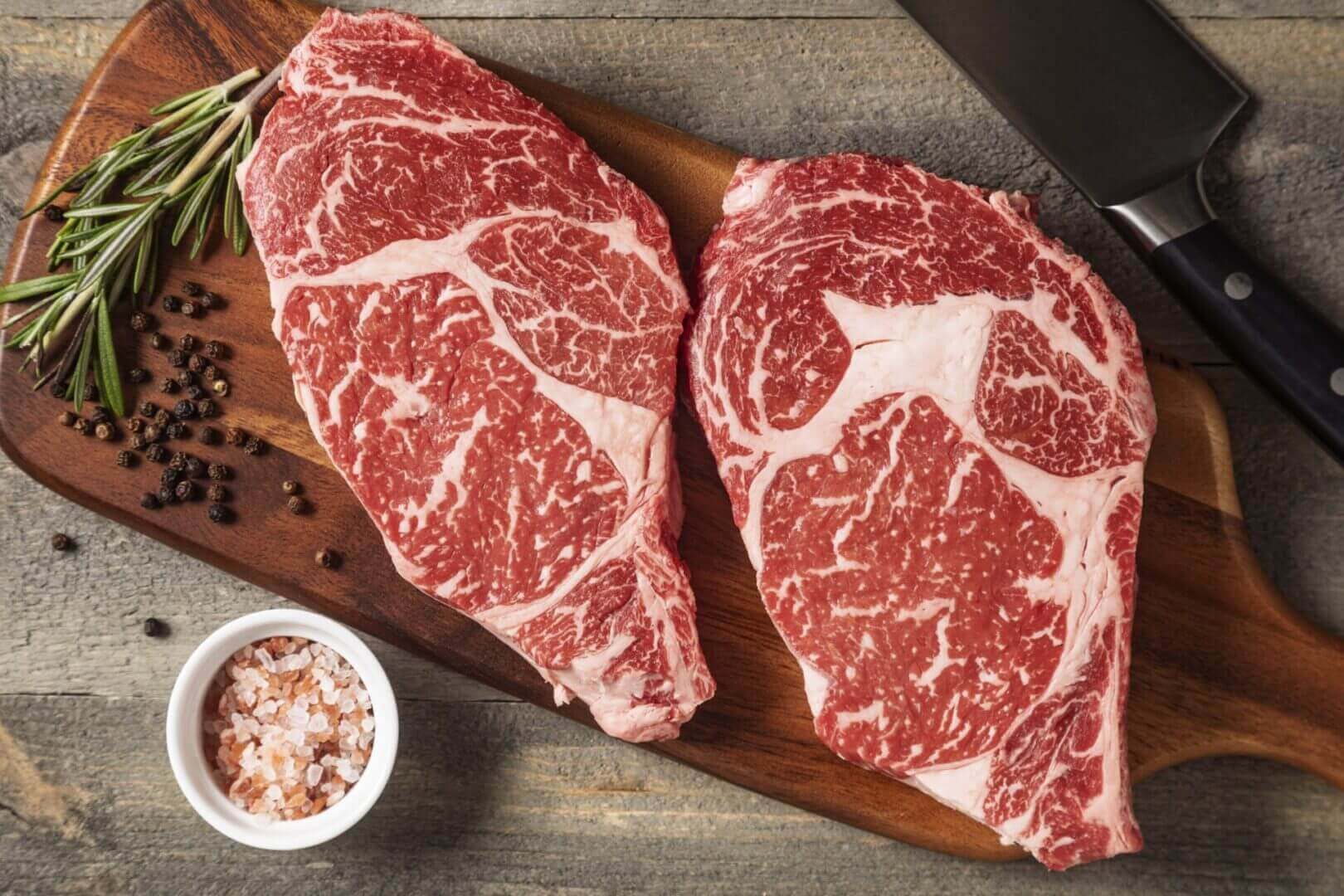 Raw ribeye steaks on wooden board