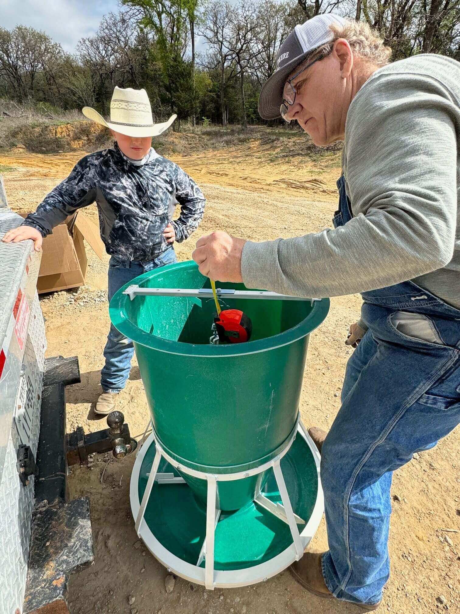 Two people inspecting green livestock feeder
